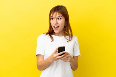 Kızıl saçlı kız sarı arka planda cep telefonuyla izole edilmiş.