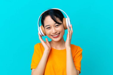 Genç Vietnamlı kadın mavi arka planda izole edilmiş müzik dinliyor.