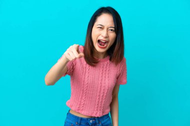 Genç Vietnamlı kadın mavi arka planda izole edilmiş hayal kırıklığına uğramış ve ön tarafı işaret ediyor.