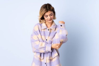 Genç Rus kadın mavi arka planda izole edilmiş, dirseğinde ağrı var.