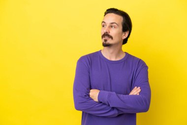 Sarı arka planda izole edilmiş genç beyaz adam yan tarafa bakıyor.