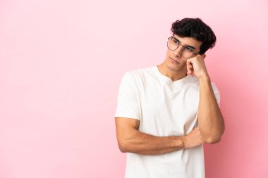 Arjantinli genç adam pembe arka planda izole edilmiş, yorgun ve sıkılmış bir ifadeyle.