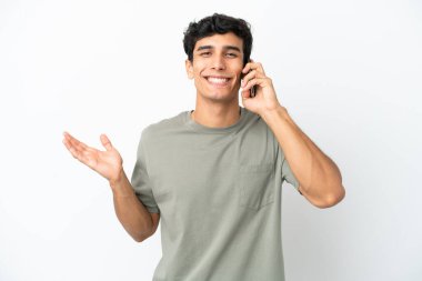 Beyaz arka planda izole edilmiş genç Arjantinli bir adam cep telefonuyla sohbet ediyor.