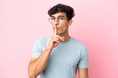 Arjantinli genç bir adam pembe arka planda gözlüklü ve sessiz hareketler yapıyor.
