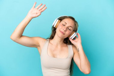 Genç beyaz kadın mavi arka planda izole edilmiş müzik ve dans dinliyor.