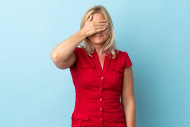 Mavi arka planda izole edilmiş orta yaşlı bir kadın gözlerini elleriyle kapatıyor. Bir şey görmek istemiyorum.