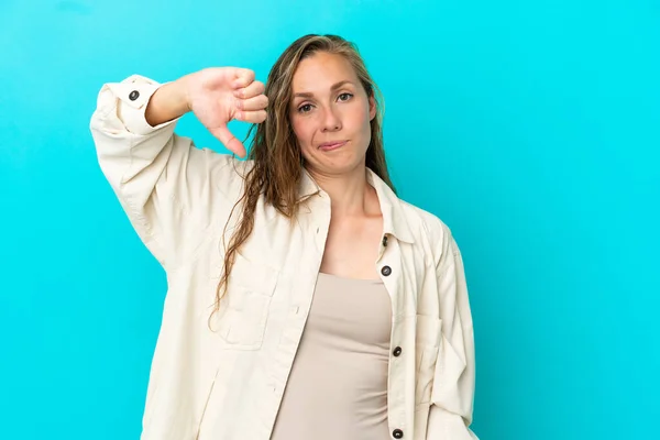 青い背景に孤立した若い白人女性は否定的な表現で親指を下に示す — ストック写真