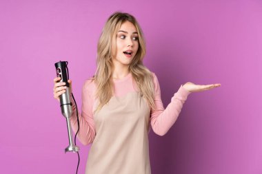 Mor arka planda izole edilmiş el blenderi kullanan genç Rus kız iki elle kopyalama alanı tutuyor.