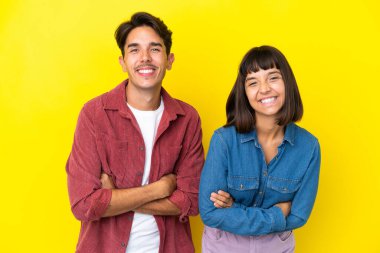 Sarı arka planda izole edilmiş genç melez çift gülümserken kollarını çapraz tutuyor.