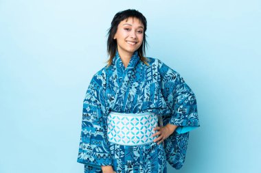 Kimono giyen genç bir kadın mavi arka planda gülüyor.