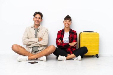 Genç melez ırk yolcuları, beyaz arka planda izole bir şekilde yerde oturuyorlar ve kollarını ön cephede kavuşturuyorlar.