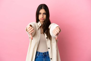 Pembe arka planda izole edilmiş beyaz bir kadın baş parmağını iki eliyle aşağı gösteriyor.