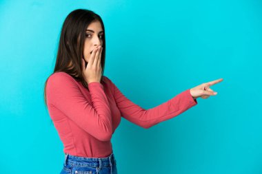 Mavi arka planda izole edilmiş beyaz bir kadın, sürpriz bir ifadeyle işaret ederken...