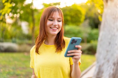 Dışarıdaki güzel kızıl saçlı kadın cep telefonuyla mesaj ya da e-posta yolluyor.