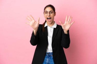 Pembe arka planda izole edilmiş beyaz iş kadını parmaklarıyla 10 'a kadar sayıyor.