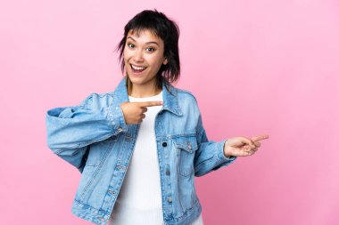 Genç Uruguaylı kadın soyutlanmış pembe arka planda şaşırmış ve işaret ediyor