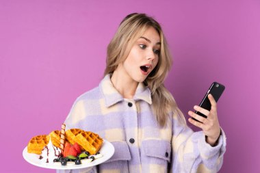 Elinde mor arka planda waffle tutan genç bir Rus kız. Elinde kahve ve cep telefonu var.
