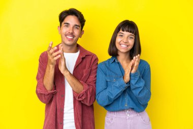 Genç melez çift sarı arka planda bir konferansta sunumdan sonra alkış tutuyorlar.