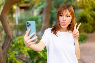 Açık havada cep telefonu kullanan güzel, kızıl saçlı bir kadın.