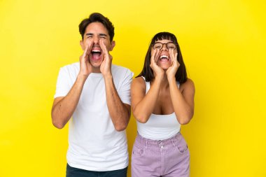 Genç melez çift sarı arka planda izole edilmiş bağırıyor ve bir şey duyuruyorlar.