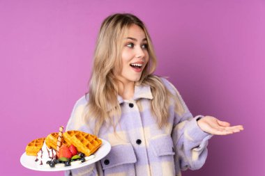 Mor arka planda yüzü sürpriz bir şekilde izole edilmiş waffle tutan Rus genç kız.