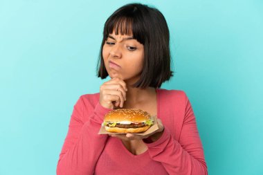 Genç esmer kadın izole edilmiş arka planda hamburger tutuyor.