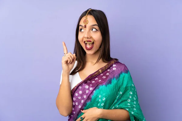 指を持ち上げながら解決策を実現しようと紫色の背景に隔離された若いインド人女性 — ストック写真