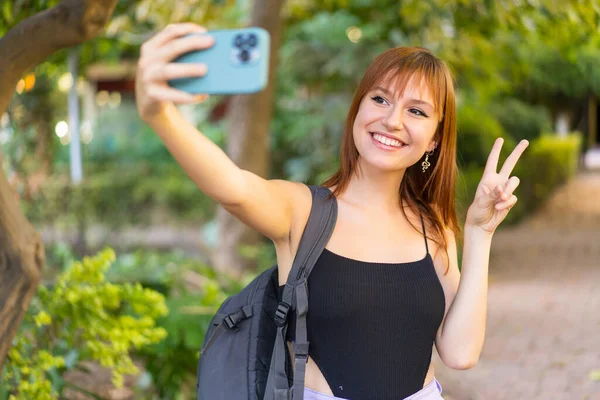 Genç, güzel, kızıl saçlı, açık havada selfie çeken bir kadın.