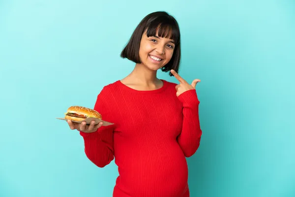 Молодая Беременная Женщина Держит Бургер Изолированном Фоне Показывая Большой Палец — стоковое фото