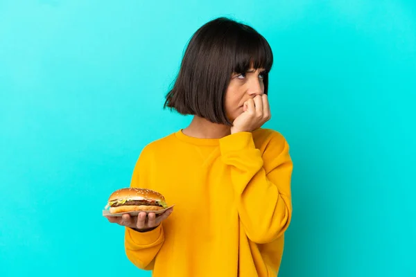 Młoda Brunetka Kobieta Trzyma Hamburgera Odosobnionym Tle Mając Wątpliwości — Zdjęcie stockowe