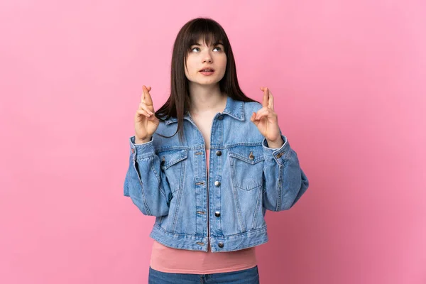 Young Ukrainian woman isolated on pink background with fingers crossing and wishing the best