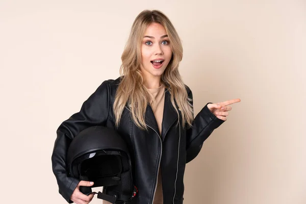 오토바이 헬멧을 러시아 소녀가 베이지 배경에서 고립되어 놀라서 방향을 가리키고 — 스톡 사진