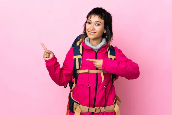 年轻的登山者女孩 背大背包 背过孤立的粉色背景 手指指向侧面 — 图库照片