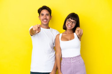 Genç melez çift sarı arka planda izole edilmiş parmaklarını kendine güvenen bir ifadeyle sana gösteriyor.