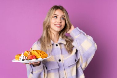 Elinde waffle tutan genç Rus kız mor arka planda izole edilmiş bir fikir düşünüyor.