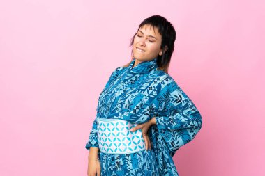 Kimono giyen genç bir kadın, izole edilmiş mavi arka planda çaba sarf ettiği için sırt ağrısı çekiyor.