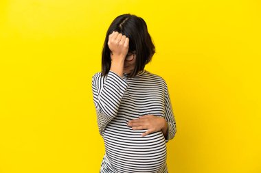 Genç hamile kadın sarı arka planda, baş ağrısı var.