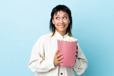 Genç Uruguaylı kadın izole edilmiş mavi arka planda elinde koca bir kova patlamış mısır tutuyor.