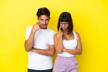 Sarı arka planda izole edilmiş genç melez çift ön tarafa bakıyor.