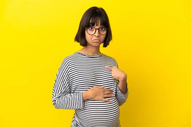 Kendini gösteren izole edilmiş sarı arka planda genç hamile bir kadın.