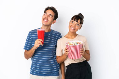 Beyaz arka planda izole edilmiş genç melez arkadaşlar ellerinde koca bir kova patlamış mısır tutuyorlar.