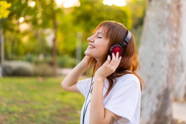 Genç, kızıl saçlı, açık havada müzik dinleyen bir kadın.