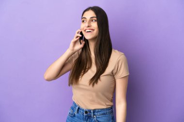 Mor arka planda izole edilmiş cep telefonu kullanan genç beyaz kadın yukarı bakarken bir fikir düşünüyor.