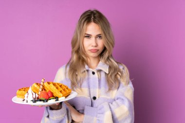 Mor arka planda izole edilmiş waffle tutan genç Rus kız üzgün