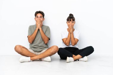 Genç melez çift, beyaz arka planda izole bir şekilde otururken ağzı kapalıyken gülümsüyor.