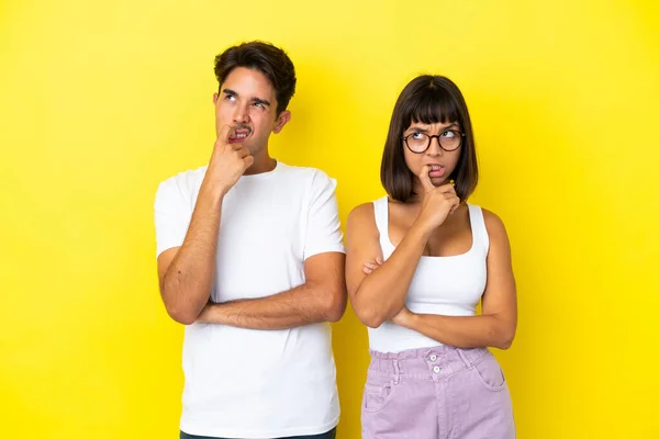 Junges Mischlingspaar Isoliert Auf Gelbem Hintergrund Mit Zweifeln Beim Nachschauen — Stockfoto