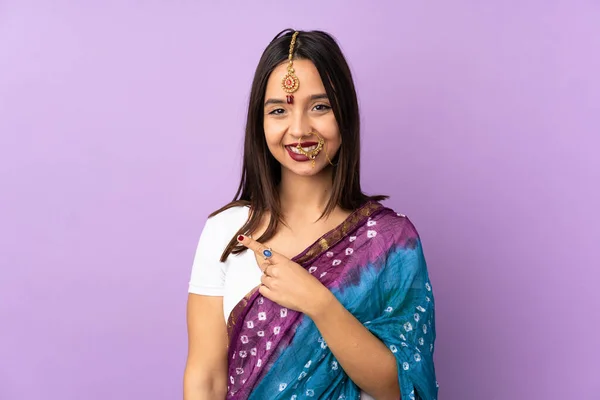 製品を提示するために側面を指す紫色の背景に隔離された若いインド人女性 — ストック写真