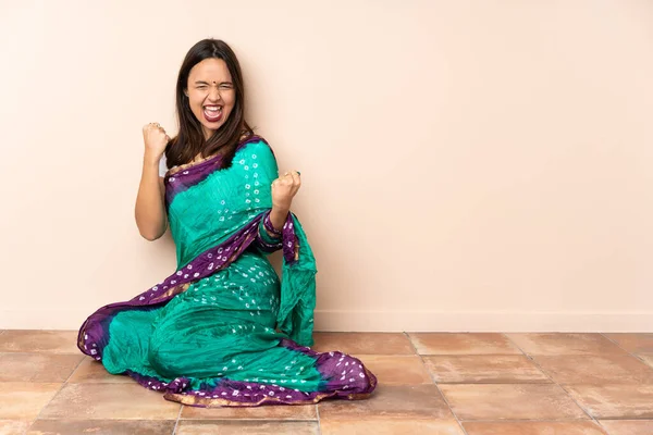 Young Indian woman sitting on the floor celebrating a victory