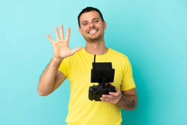 İzole edilmiş mavi arkaplan üzerinde uzaktan kumanda tutan Brezilyalı adam parmaklarıyla beşi sayıyor.