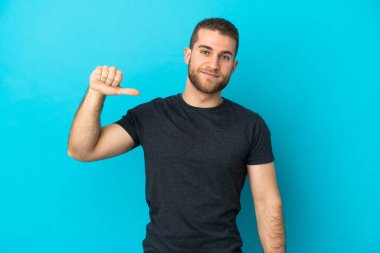 Mavi arka planda soyutlanmış yakışıklı beyaz adam gururlu ve kendini beğenmiş.